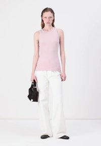 Débardeur sans manches rose pâle associé à un pantalon large blanc. Tenant un petit sac à main noir. Matériau lisse sur l'ensemble.