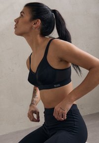 Svart sportsbh med justerbare stropper, med et teksturert meshdesign og ribbet bånd. Komplimenteres av svarte høytlivs leggings.