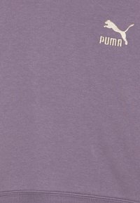 Lilla pusakirja, millel on tekstuuriga kangas, soonikuga äär ja tikitud Puma logo ülemisel vasakul küljel.