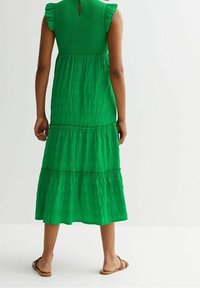 Grön, lager-på-lager klänning med smocksydd bodice och fladdrande ärmar, med en nyckelhålsöppning bak och mjukt, texturerat tyg. Sandal skor.