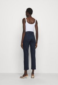 Hoger-gesneden donkerblauwe jeans met rechte pijpen, gecombineerd met een wit tanktop. De outfit heeft een cropped ontwerp en een slanke pasvorm.