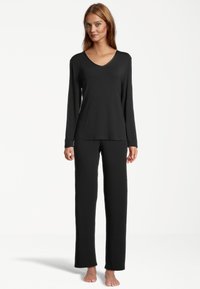 Schwarzes Langarm-V-Ausschnitt-Oberteil, kombiniert mit passenden weit geschnittenen Hosen, aus weichem Stoff mit glatter Textur und minimalen Nähten.