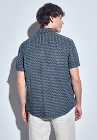 Short-sleeve shirt featuring a dark blue pattern with geometric designs, a button-down collar, and a curved hem. Made from lightweight fabric.