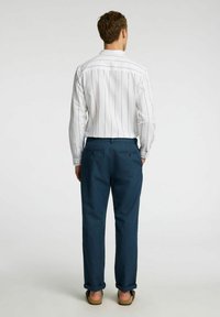 Vitrandig långärmad skjorta med knapp-ner krage, matchad med mörkblå byxor. Byxorna har två bakfickor med knappar.