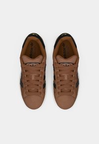 Rudi sportiniai bateliai su lygiu paviršiumi, juodomis juostelėmis ir raišteliais, balta pada, o liežuvėlyje auksinė logotipo detalė.