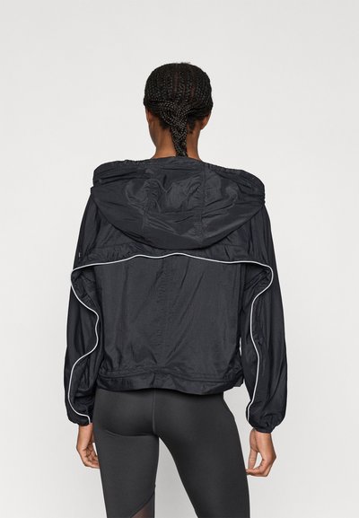 Μαύρο αδιάβροχο μπουφάν με κουκούλα, με λευκές λεπτομέρειες κατά μήκος των ραφών και ελαστικές μανσέτες, εμφανιζόμενο από πίσω.