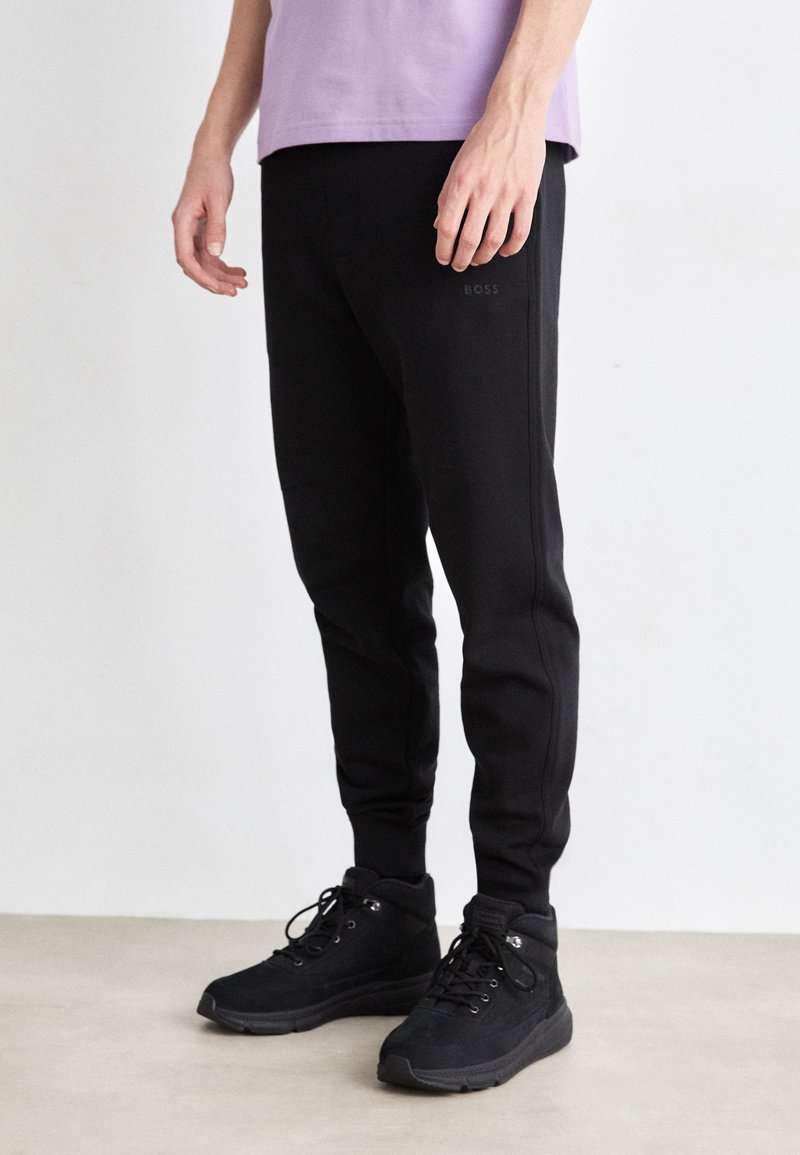 Zwarte joggerbroeken van zachte stof, met een slimfit ontwerp en een logo op de dij, gecombineerd met zwarte hoge sneakers.