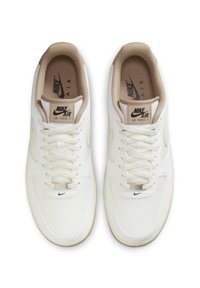 Tenisky Nike Air Force 1 s bílým koženým svrškem, texturovanými akcenty, béžovou podšívkou a plochými tkaničkami. Obsahují logové nášivky na jazyku a na boku.