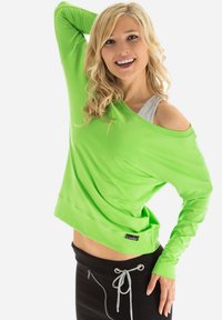 Sweatshirt vert lime avec un design dégageant les épaules, manches longues et coupe ajustée, associé à un pantalon de jogging noir à cordon de serrage avec des accents argentés.