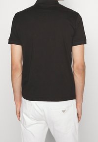 Svart pikétröja med klassisk passform, korta ärmar och krage. Bärs med vita denimbyxor med logotypdetalj på bakfickan.