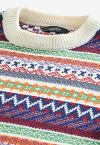 Gros plan sur le col d'un pull tricoté avec des motifs géométriques multicolores en violet, vert, orange, rouge et blanc, avec une étiquette de la marque NEXT.