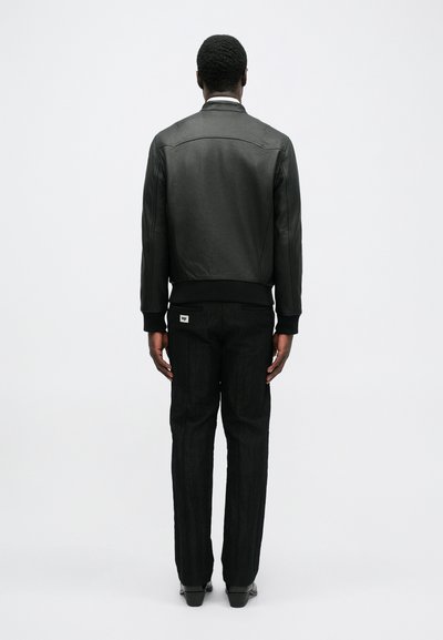 Černá kožená bomber bunda s ribbed lemem, která má hladkou texturu a minimalistický design. Spárovaná s texturovanými černými kalhotami.