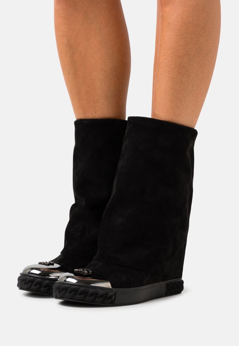 Botines de ante negro con diseño plegado, punta redondeada y detalles metálicos. Presentan una textura trenzada en la suela.