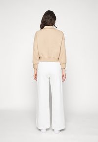 Beige kort sweatshirt med krage och sänkt axel, kombinerad med vida vita byxor. Slät bomullstextur, minimalistisk design.