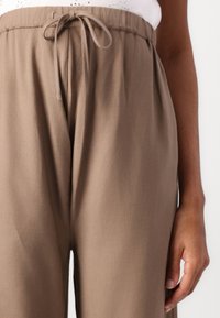 Pantalons légers marron avec une taille élastique et un cordon de serrage. Présentent une texture lisse et une coupe fuselée, adaptés à un style décontracté.