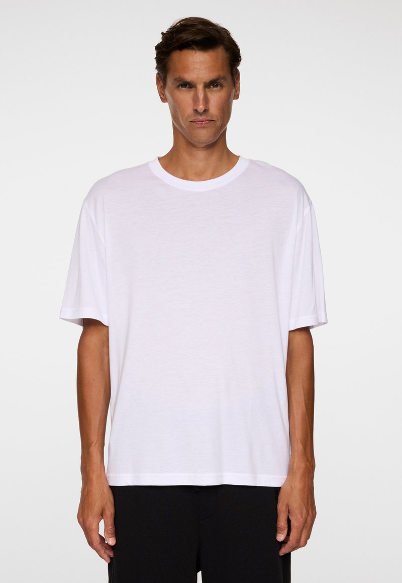 Vit bomullströja med rund halsringning, korta ärmar och avslappnad passform, med en slät textur och minimala detaljer.