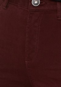 Bordowy materiał dżinsowy z srebrnym guzikiem i widocznym przeszyciem wokół przedniej kieszeni oraz obszaru paska.