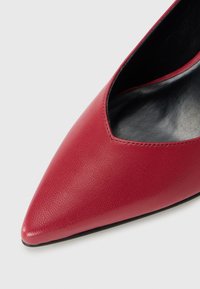 Red leather pointed-toe shoe with a low-cut front, smooth texture, and a black inner lining, featuring minimal stitching detail.