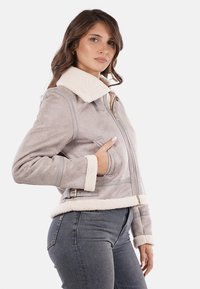 Giacca in ecopelle grigia con un caldo colletto e polsini in shearling bianco, dotata di zip frontale e tasche laterali. Design strutturato e aderente.