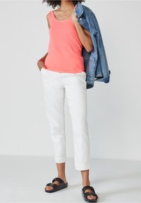 Débardeur corail, pantalon blanc raccourci et sandales noires. Veste en denim posée sur l'épaule. Design simple et coupe décontractée.