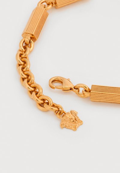Βραχιόλι από χρυσό με κούμπωμα αστραγάλου, διαθέτει υφασμένο ορθογώνιο κρίκο και μικρό μενταγιόν κεφάλι λιονταριού προσαρτημένο στην αλυσίδα.