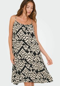 Zwart en beige patroon jurk met een losse pasvorm, spaghettibandjes en een vloeiende silhouet, met een geometrisch ontwerp overal.
