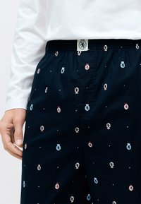 Shorts de salon bleu marine avec une taille à cordon, arborant un motif répétitif de badges en rouge, bleu et blanc avec de petits points blancs.