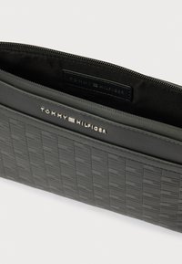 Μαύρο πορτοφόλι από δερματίνη με υφή και υφαντό μοτίβο εμπρός, με κλείσιμο με φερμουάρ και ασημένιο ανάγλυφο λογότυπο στο εξωτερικό μέρος.