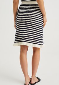 Stickad pennkjol designad med marinblå och krämfärgade horisontella ränder, med en ribbad midja och en volang nederkant.