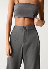 Top court gris en tissu lisse avec des bretelles fines, associé à un pantalon gris taille haute avec une fermeture à un bouton et des plis.