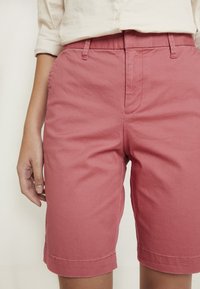 Shorts en coton rose à coupe droite, avec poches latérales, passants pour ceinture et détails de couture subtils, se terminant juste au-dessus du genou.