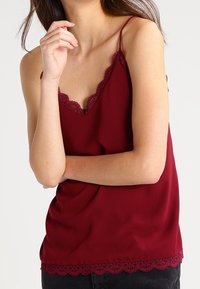 Burgundy linne med spetsdetaljer vid halsringningen och fållen. Tillverkad av ett smidigt tyg, med tunna justerbara axelband och en avslappnad passform.