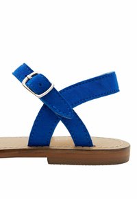 Sininen mokkainen sandaali, jossa on ristikkäiset hihnat, säädettävä hopeinen solki ja litteä puupohja ompelu koristeluilla.