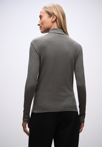 Un top grigio a maniche lunghe con colletto alla cinese. Materiale morbido, design aderente e texture liscia. Indossato con pantaloni neri, vista da dietro.
