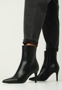 Stivaletti neri con tacco alto, realizzati in pelle texturizzata, punta affusolata e tacco sottile. Presentano una silhouette liscia ed elegante e una chiusura con zip.