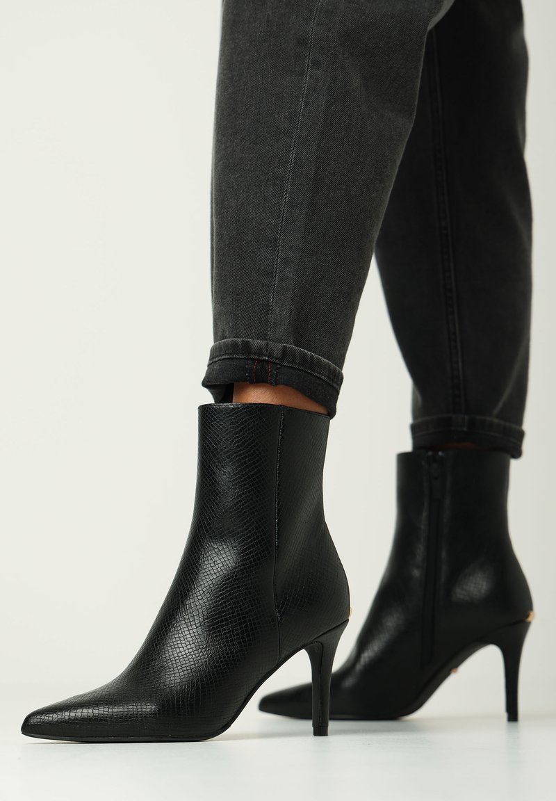 Stivaletti neri con tacco alto, realizzati in pelle texturizzata, punta affusolata e tacco sottile. Presentano una silhouette liscia ed elegante e una chiusura con zip.