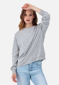 Pull gris en maille avec un col rond, des manches longues raglan et des poignets côtelés. Associé à un jean en denim bleu clair.