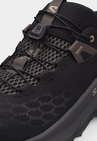 Μαύρο και γκρι παπούτσι για τρέξιμο στο μονοπάτι Salomon Ultra Glide 4 με επάνω μέρος από διχτυωτό υλικό, σύστημα γρήγορου δέσιμου και υφή στην σόλα.