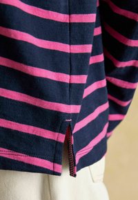 Tume sinine ja roosa triibuline puuvillane särgiga, küljevahesein ja kontrastsete õmblustega hemil. Pehme tekstuur ja vabaaja sobivus.