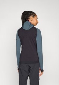 Schmal geschnittener Hoodie in Schwarz mit blauen Ärmeln und Kapuze, ausgestattet mit einem rosa Innenfutter. Strukturierter Stoff mit Daumenlöchern und einem dezenten Logodesign.
