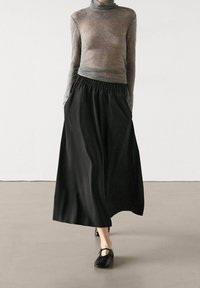 Gonna lunga nera con cintura elastica, abbinata a un maglione a collo alto grigio aderente. Tessuto morbido, design semplice. Indossate ballerine nere.