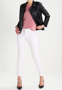Zwarte faux leren jas met drukknoopsluitingen, roze top met korte mouwen, witte skinny jeans en zwarte hoge hakken. Glad textuur, moderne pasvorm.