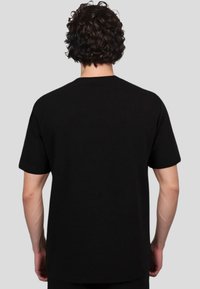 Zwarte katoenen T-shirt met korte mouwen, relaxte pasvorm, naadloze schouderconstructie en een zachte textuur. Achteraanzicht weergegeven.