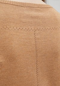 Maglione color marrone chiaro, lavorato a maglia, con scollo rotondo e cuciture decorative con piccoli fori lungo la cucitura per una maggiore texture.