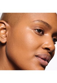 Primer plano de una piel de tono marrón claro y suave con textura sutil, destacando una oreja y una línea de mandíbula bien definida, y un color natural de labios.