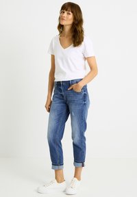 Camiseta blanca con escote en V combinada con vaqueros desgastados azul claro y zapatillas blancas. Los vaqueros tienen bajos enrollados y bolsillos.