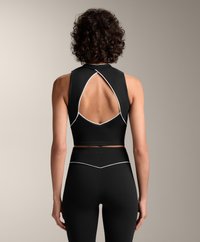 Musta urheilullinen crop-top, jossa on avokelkkataustasuunnittelu ja valkoiset yksityiskohdat, yhdistettynä korkeavyötäröisiin mustiin leggingseihin. Sujuva, joustava materiaali.