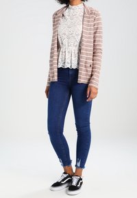 Veste à rayures pêche sur un haut en dentelle blanche avec peplum, associée à un jean skinny bleu foncé et des baskets noir et blanc.