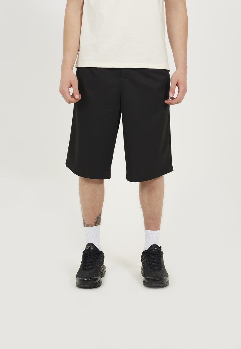 Black athletic shorts made of breathable fabric, featuring a loose fit and smooth texture, paired with black sneakers and white socks.