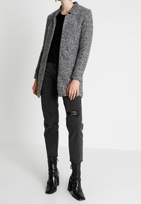 Abrigo gris jaspeado con cuello, top negro de canalé, jeans negros con un desgarro y botas de tobillo negras brillantes. Diseño simple y moderno.